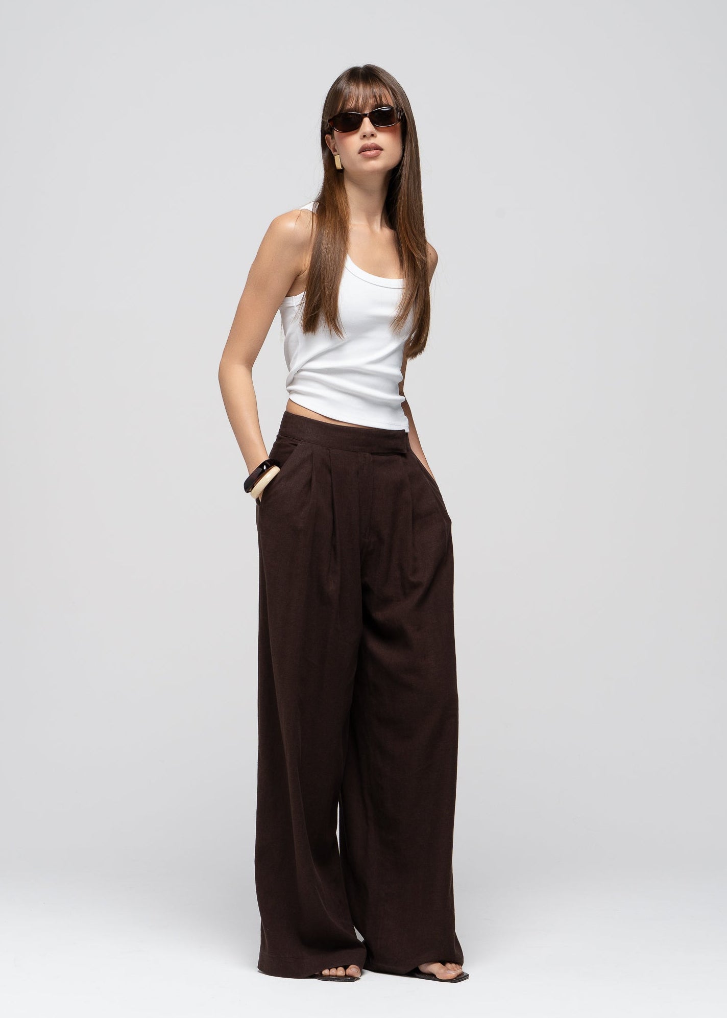 Woman wearing a white top and brown wide-leg pants on a white background